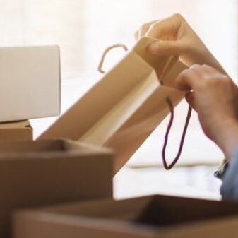 a woman opening and looking inside shopping bag with postal parcel box on the table at home for delivery and online shopping concept